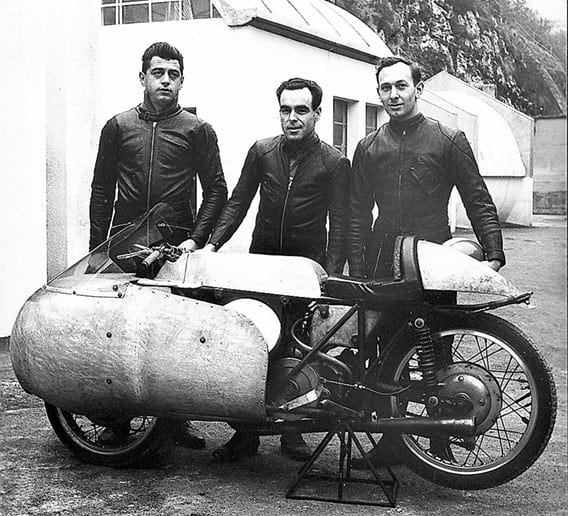 Het fabrieksraceteam van Moto Guzzi voor de windtunnel van de fabriek in maart 1955. Van links naar rechts Duilio Agostini, Ken Kavanagh en Dickie Dale. De afgebeelde motorfiets is overigens een ééncilinder raceprototype. (Published with kind permission of Ken Kavanagh)